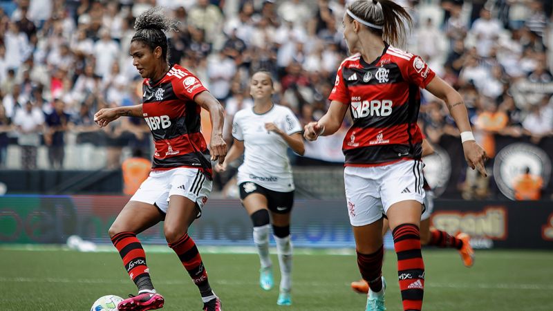 Jogadoras do Flamengo com a camisa rubro-negra disputam a bola contra o Corinthians em jogo do futebol feminino
